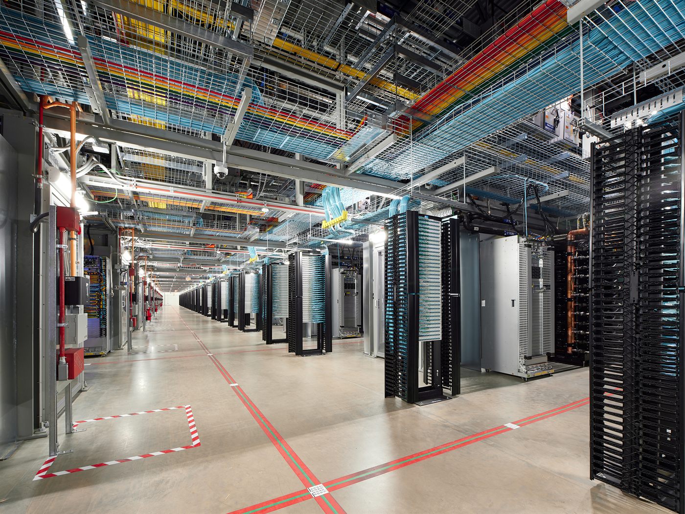 A Google data center hallway in Council Bluffs, Iowa, with colorful fiber-optic cable trays running overhead between rows of server racks.